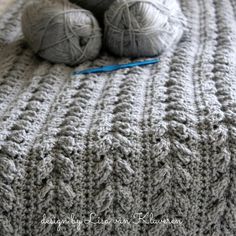 two balls of yarn sitting on top of a gray crocheted blanket next to a ball of knitting needles