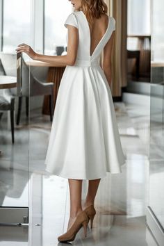 a woman in a white dress is standing near a glass wall and looking into the distance