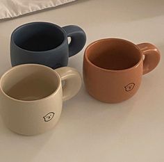 three coffee mugs sitting next to each other on a white counter top, one is blue and the other has brown