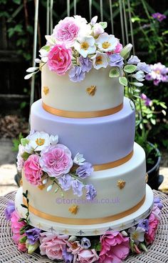 a three tiered cake with flowers on the top and bottom is sitting on a wicker table