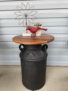 a bird statue sitting on top of a wooden table next to a black vase with a plant in it