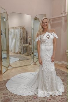 a woman standing in front of a mirror wearing a wedding dress with off the shoulder sleeves