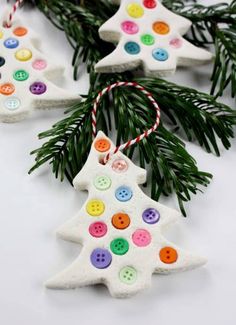 three decorated christmas tree ornaments hanging from a pine branch with colorful buttons on them and twine of yarn