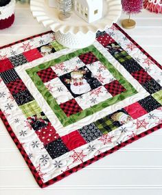 a quilted table runner with a house on it and christmas decorations around the edge