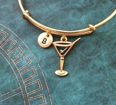 a close up of a gold bang bracelet with a charm and initial charms on it