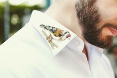 a man with a beard wearing a white shirt and embroidered bird on his lapel