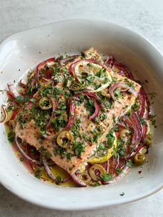 a white bowl filled with fish and vegetables on top of a table next to a fork