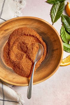 a wooden bowl filled with spices next to sliced oranges and leaves on a table