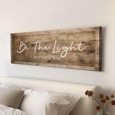 a wooden sign that says be the light above a bed