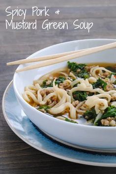 a white bowl filled with noodles and greens next to chopsticks on a plate