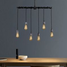 a wooden table topped with a bowl and light bulbs hanging from it's ceiling