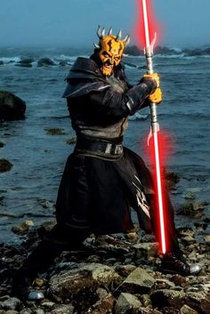 a man dressed as darth vader holding a lightsaben on the beach