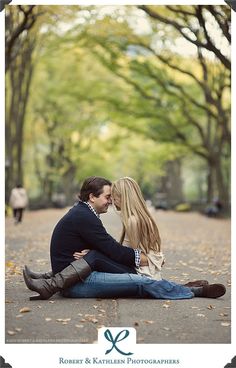 a man and woman are sitting on the ground in front of trees with their arms around each other