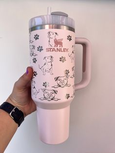 a person holding a pink travel mug with dogs on it and the words stanley printed on it