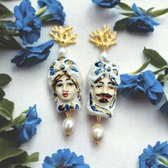 "Pendant earrings with Sicilian Moors in Sicilian Caltagirone ceramic. These Sicilian earrings are handmade jewels in Sicily and in Sicilian style with the use of oven-glazed ceramic and finishes with gold leaf decorations. The ceramic element depicts \"the couple of Moors\", also called \"Sicilian Moors\" and \"Sicilian heads\", they are legendary characters of Sicilian culture. Hypoallergenic earrings with gold plated brass earring, in the shape of a coral branch, pin and butterfly closure. It is possible to choose the color of the stone you prefer among the proposed variants: - Rose, cherry rose quartz - Turquoise, turquoise paste - White and Blue, pearl Measure total length about 8 cm (3.14 Inch) Measures width of brown about 2.5 cm (0.98 Inch) All the materials used are hypoallergenic Handmade Mediterranean Jewelry For Gift, Sicilian Jewelry, Sicilian Culture, Sicilian Style, Italian Gifts, Handmade Jewel, Italian Ceramics, Leaf Decor, Hypoallergenic Earrings