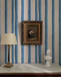 a painting is hanging on the wall next to a table with a lamp and busturine