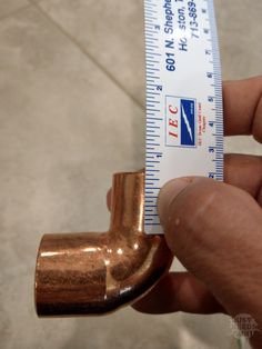 a person is holding a measuring tape and a copper colored pipe on the tile floor