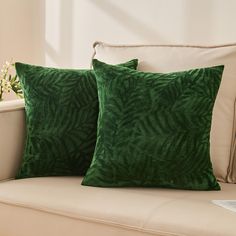 two green pillows sitting on top of a couch next to a vase filled with flowers