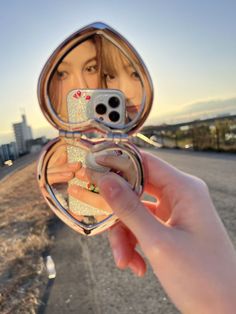 a woman taking a selfie with her cell phone in a compact mirror on the street