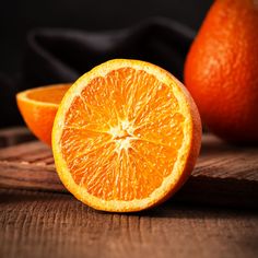 an orange cut in half sitting on top of a wooden cutting board next to two oranges