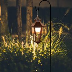 an old fashioned lamp in the middle of some tall grass and trees at night time