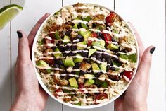 two hands holding a bowl filled with rice, beans, avocado and dressing