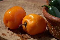 two orange peppers sitting on top of a wooden cutting board next to a potted plant