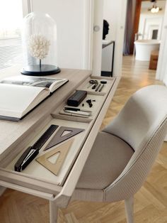 a desk with an open book, pen and notebook on it next to a chair