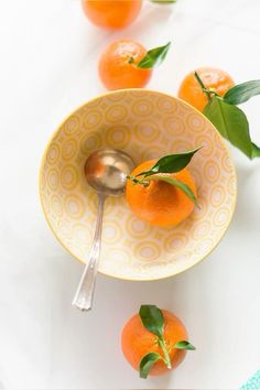 an orange sitting in a bowl with a spoon next to it on a white table