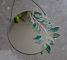 a mirror with green leaves on it sitting next to a leafy branch and wire