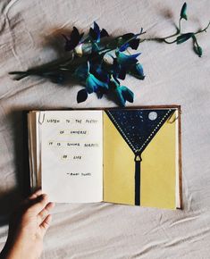 someone is holding an open book with writing on it next to some flowers and leaves