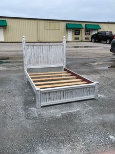 a white bed frame with wooden slats in an empty parking lot