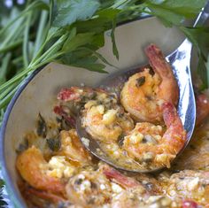 a bowl filled with shrimp and vegetables on top of a green table cloth next to a spoon