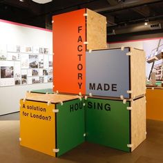 three different colored boxes stacked on top of each other in an exhibition room with pictures behind them