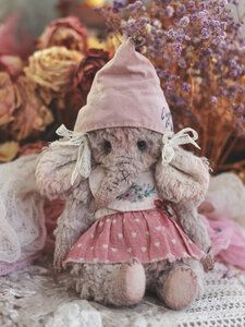 a teddy bear wearing a pink dress and hat sitting on a table next to flowers