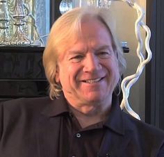 an older man with blonde hair smiling for the camera in front of a glass sculpture