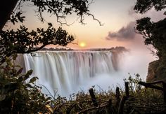 the sun is setting over a large waterfall