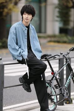 a man sitting on a rail next to a bike and wearing a blue jacket with black pants