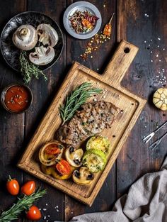 a wooden cutting board topped with meat and veggies next to other food items