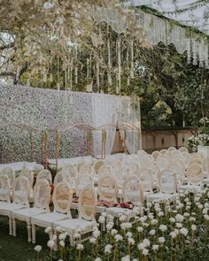 rows of white chairs sitting next to each other in front of a wall covered with flowers