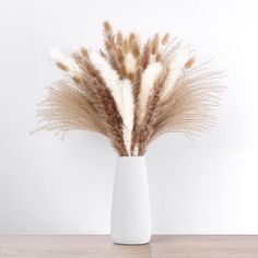 some dry grass in a white vase on a table