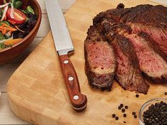 a large piece of meat sitting on top of a cutting board next to a salad