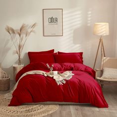 a bed with red sheets and pillows in a white room next to a table lamp