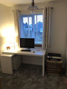 a white desk with a computer on it in front of a window and some blinds