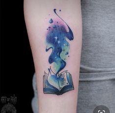 a woman's arm with a book and stars in the sky tattoo on it