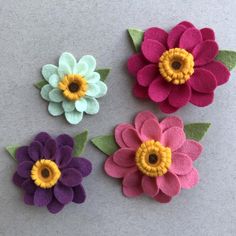 four felt flowers with green leaves and yellow center sitting on a gray surface, ready to be made into brooches