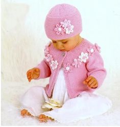 a baby girl wearing a pink knitted sweater and hat with flowers on it's head