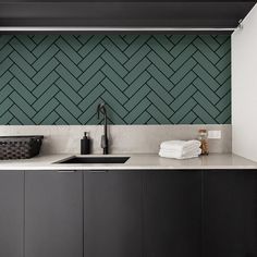 a kitchen with black cabinets and white counter tops next to a green herringbone wall