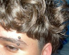 a close up of a young man with his hair in the air and piercings on his forehead