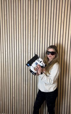 a woman wearing sunglasses holding a printer in front of a wall with vertical stripes on it